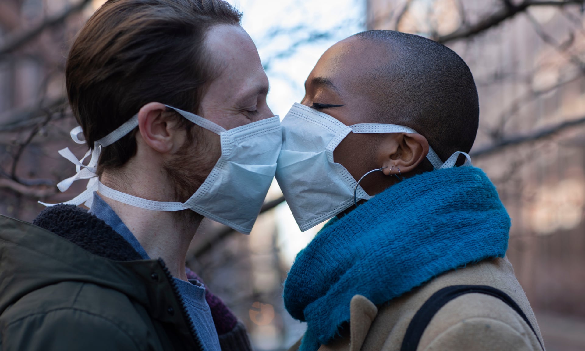 A man and a woman wearing medical masks over their noses and mouths kiss tenderly.